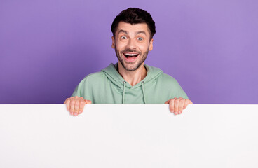 Photo portrait of nice young man excited stand behind white wall banner wear trendy gray garment isolated on violet color background