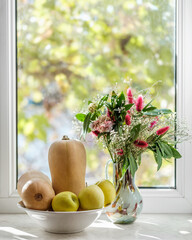 Autumn composition, bouquet of flowers in a vase, butternut squashes, apples in a bowl against...