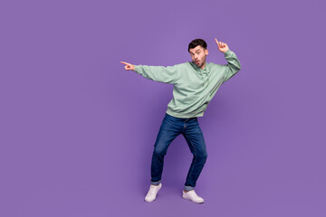 Fototapeta na wymiar Full length photo of young funny excited student businessman dancing finger pointing empty space good news celebrate isolated on violet color background