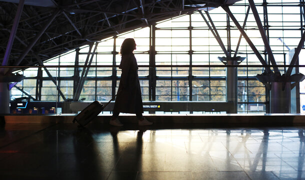 Beautiful woman with a suitcase at the airport is waiting for her departure. Migration and travel concept.