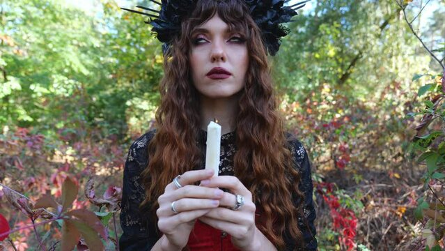 Portrait of a fabulous woman in a carnival costume holding a candle in her hands near the yellow autumn foliage. View through a candle at a woman. Magic woman. woman halloween