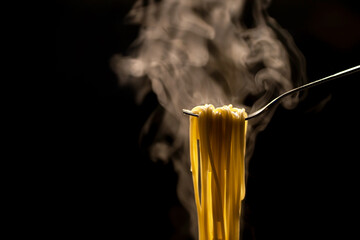 Hot steaming spaghetti hanging on a fork with a black background