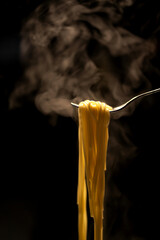 Hot steaming spaghetti hanging on a fork with a black background