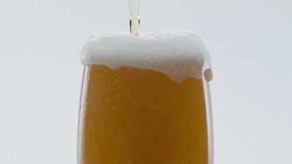 Bubbling beer foam overflowing from glass in super slow motion close up.