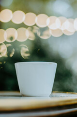 Vertical close up coffee cup on outdoor terrace table with bokeh Christmas lights