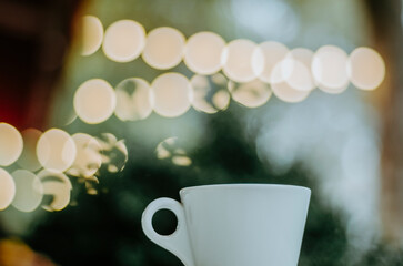 Low angle coffee cup on outdoor terrace table with bokeh Christmas lights background