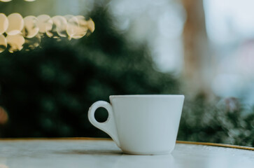 Coffee cup on outdoor terrace table with bokeh Christmas lights background