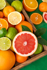 Different citrus fruits with leaves in a wooden box on a concrete background. Healthy food. Top view