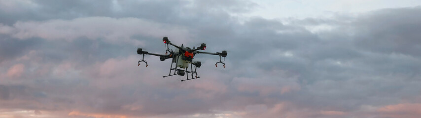 WIDE view of a huge intelligent agriculture drone with spray nozzles flying against sky early in the morning