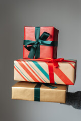 Woman's hand holds a stack of beautifully wrapped Christmas presents.