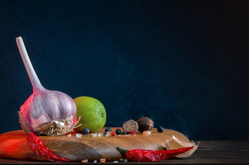 Whole Bulb Garlic, Lime, And Spices: Chili, Juniper Berries, Black, White And Pink Pepper On A Wooden Board. Kitchen Still Life. Condiments And Traditional Medicine. Dark Background. Place For Text.