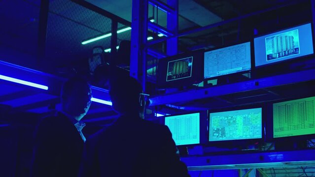 Engineers , partners , architects or businessmen in black suits discussing , analyzing , looking or watching project . A lot of monitors inside dark place . Concept of security systems or engineering