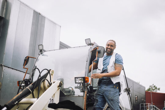 Low angle view of male construction standing at doorway of vehicle