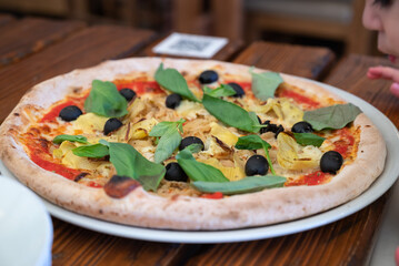 Fresh pizza with artichokes, black olives and basil leaves
