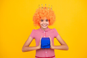 Funny princess in wig and crown. Portrait of teenager child girl 12, 13, 14, years old holding Christmas gift box. Teen giving birthday gift.