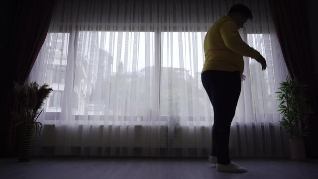 Weight problem. Unhappy obese person.
Unhappy obese person walking in front of window at home.

