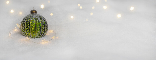 close-up of a green icy christmas ball decoration in white snow background with blurry lights,...