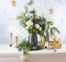Christmas decorations, candles, gift boxes and flower bouquet. Winter arrangement with roses, fir branches, winter berries. Christmas still life.
