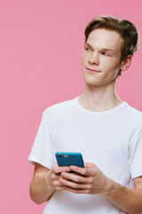 a handsome red-haired guy in a white T-shirt stands with a phone in a blue case in his hands