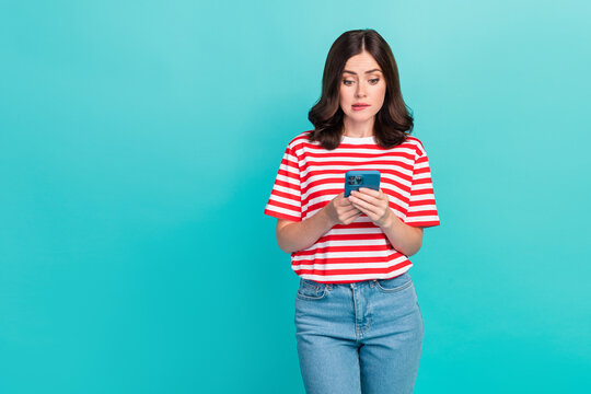 Photo of unsure uncertain girl dressed red t-shirt biting lip reading modern gadget empty space isolated teal color background