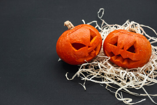 Two small carved pumpkins, on a black background.