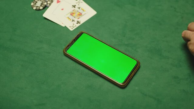 Poker players sitting near table and using mobile phone with green screen . man holding phone during game . Mobile phone on poker table . Concept of betting or online casino games .
