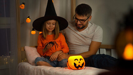 Halloween. Happy family, father and little daughter in witch black hat play with orange pumpkin lantern and spider in dark.