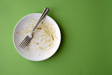 White ceramic plate with food leftover, pasta, olive oil, sauce and fork on green background. Creativity picture with space for text