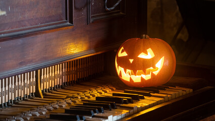 Halloween pumpkin lantern with scary face glowing inside. Decoration. Old piano. Gothic concept.