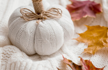 White knitted pumpkin, autumn leaves and a white knitted plaid. Stylish, warm, cozy autumn concept.
