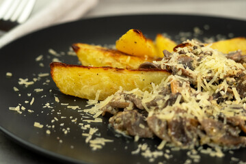 Plate of baked potatoes and mushrooms sprinkled with permesan cheese. Champignons. Food background.