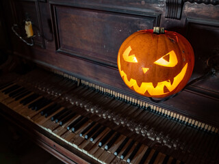 Fototapeta na wymiar Halloween pumpkin lantern with scary face glowing inside. Decoration. Old piano. Gothic concept.