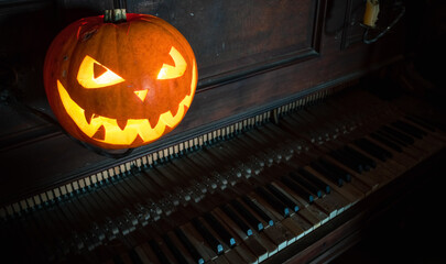 Halloween pumpkin lantern with scary face glowing inside. Decoration. Old piano. Gothic concept.