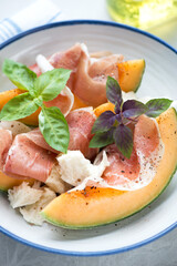 Slices of cantaloupe melon served with prosciutto ham, mozzarella and fresh basil leaves, close-up, vertical shot, selective focus