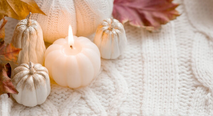 Fototapeta na wymiar Still-life. Knitted pumpkin, autumn leaves, white knitted plaid and a burning candle in the shape of a pumpkin. Cozy autumn concept.