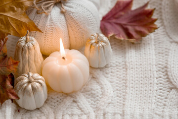 Still-life. Knitted pumpkin, autumn leaves, white knitted plaid and a burning candle in the shape of a pumpkin. Cozy autumn concept.