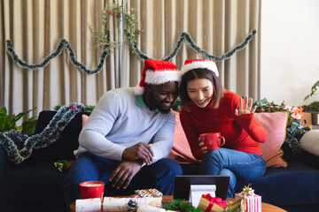 Happy diverse couple wearing santa claus hats, using tablet for video call