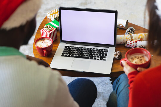 Happy diverse couple wearing santa claus hats, using laptop with copy space - Powered by Adobe