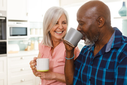 Happy Senior Diverse Couple Drinking Coffee In Kitchen