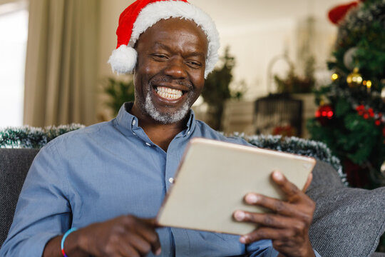 Happy senior african american man with santa hat using tablet