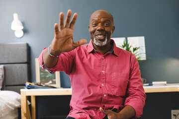 Happy african american senior man making video call at home smiling and waving to camera