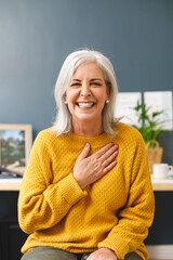 Vertical image of happy caucasian senior woman making video call smiling to camera, touching chest - obrazy, fototapety, plakaty