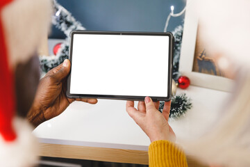 Diverse senior couple in santa hats making christmas video call holding tablet, copy space on screen