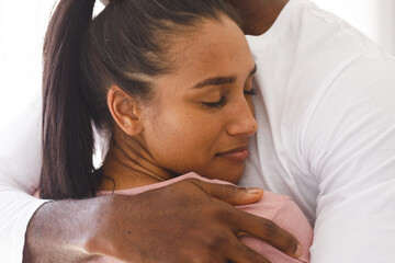 Happy diverse couple embracing by window at home, woman smiling