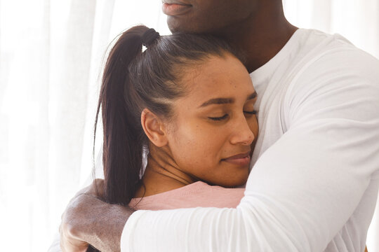 Happy Diverse Couple Embracing By Window At Home, Smiling