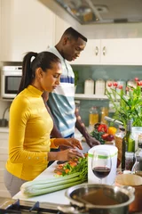  Vertical image of diverse couple preparing food together, washing and chopping vegetables in kitchen © WavebreakMediaMicro