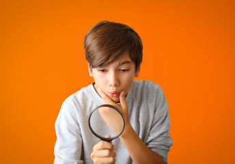 Curious young boy with magnifying glass Isolated on orange color background. Surprised school boy student looking through magnifying glass.