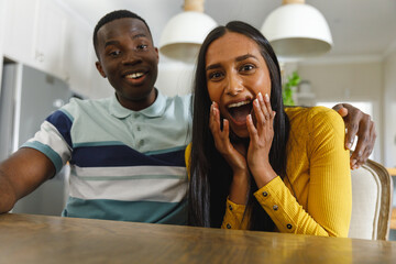 Happy diverse couple making video call smiling and laughing to camera in kitchen