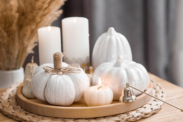 Still-life. Knitted pumpkin, pampas grass, pumpkin-shaped candles and white ceramic pumpkins on a wooden tray on a coffee table in the home interior of the living room. Cozy autumn concept.
