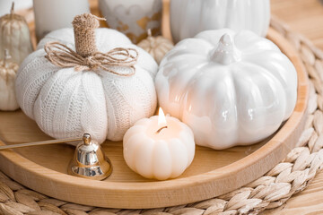 Still-life. Knitted pumpkin, pampas grass, pumpkin-shaped candles and white ceramic pumpkins on a wooden tray on a coffee table in the home interior of the living room. Cozy autumn concept.